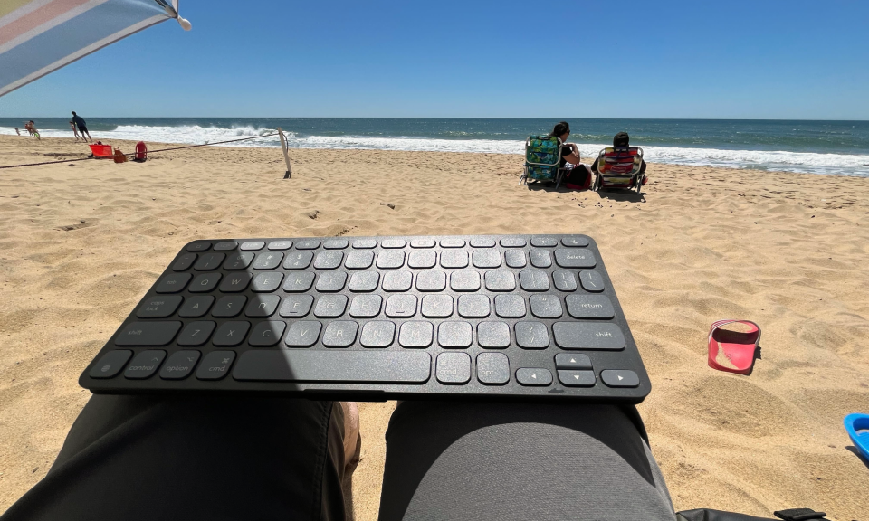 A Logitech Keys-To-Go 2 keyboard resting on a person's lap while on the person is on the beach.