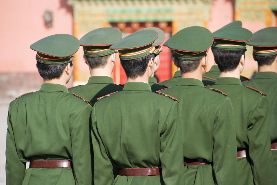 Unrecognizable group of soldiers standing in line and seen from behind. Wearing uniforms including caps. The soldiers belong to the Chinese armed forces.