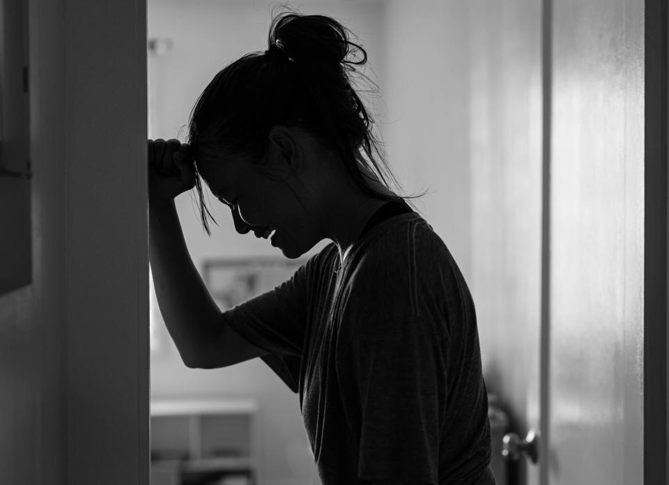 Silhouette of a person leaning against a wall, seemingly in a moment of stress or contemplation, in a dimly lit room