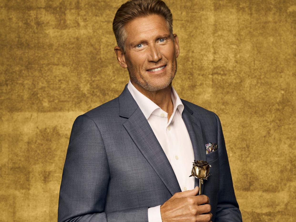 Gerry Turner smiles in a gray suit and white shirt while holding a golden rose.