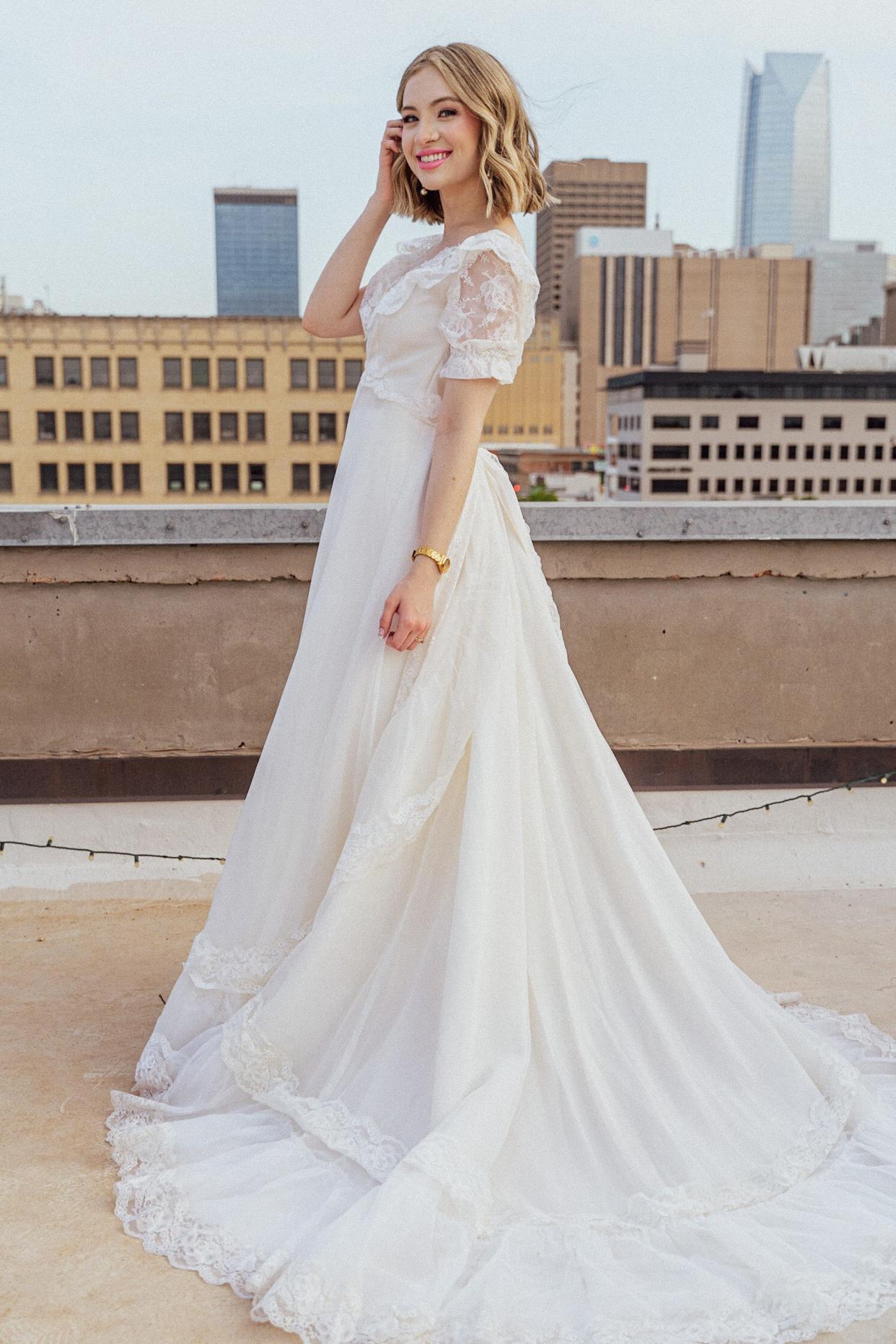 A bride smiles in her wedding dress on top of a roof.