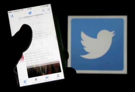 FILE PHOTO: A man reads tweets on his phone in front of a displayed Twitter logo in Bordeaux, southwestern France, March 10, 2016. REUTERS/Regis Duvignau/Illustration/File Photo