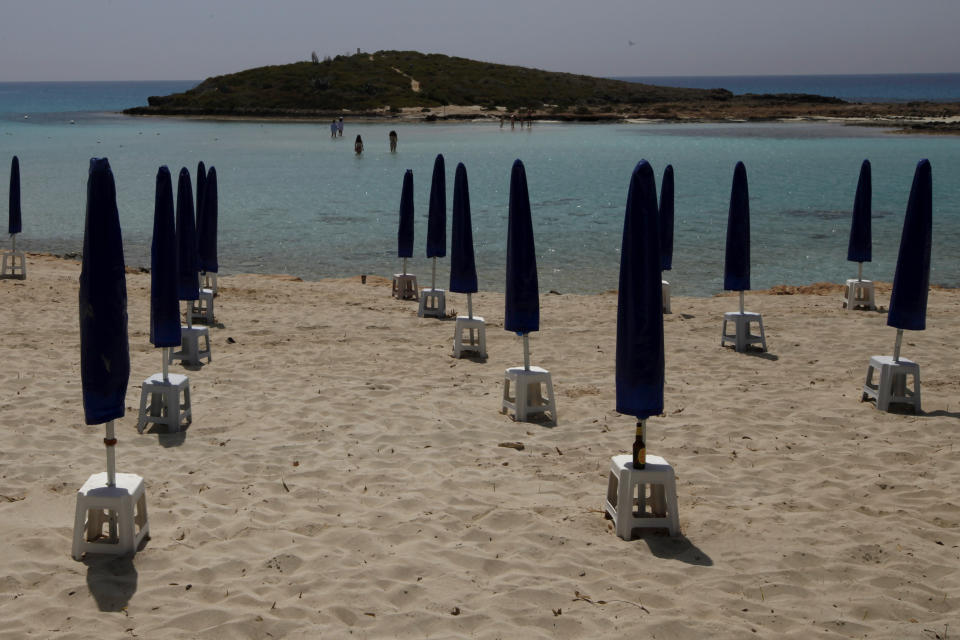 Rows of closed parasols on a nearly empty stretch of Nissi beach with a few beachgoers in the distance in Cyprus' seaside resort of Ayia Napa, a favorite among tourists from Europe and beyond, on Wednesday, May 13 2020. With coronavirus restrictions gradually lifting, Cyprus authorities are mulling ways to get holidaymakers back to the tourism-reliant island nation that officials say is estimated to lose 70% of its annual tourist arrivals. (AP Photo/Petros Karadjias)