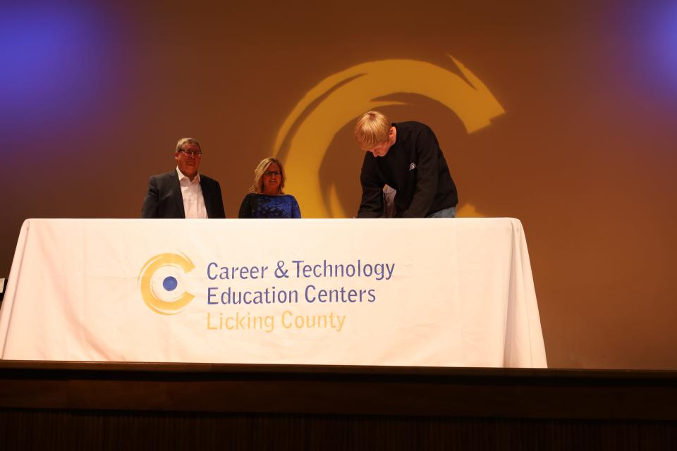 A C-TEC senior signs an apprenticeship with a local company last week during a ceremony at the school, as Heath-Newark-Licking County Port Authority president and CEO RIck Platt, and Licking County Chamber of Commerce president Jennifer McDonald look on. Fifty-four seniors signed with over 20 local companies in front ot family and the student body.