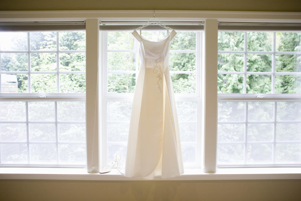 Wedding dress hanging in front of windows with greenery outside