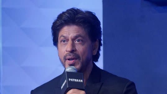 shah rukh khan sitting in a chair on stage and talking to an audience with a microphone