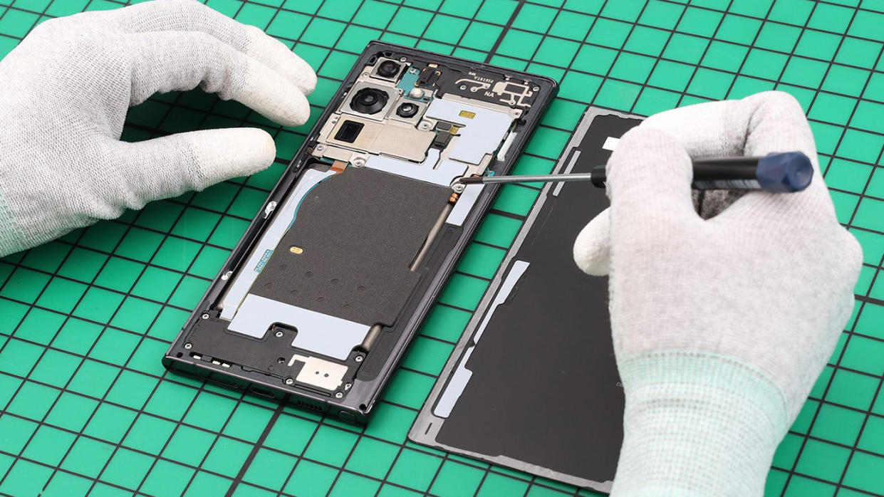  Two hands in white gloves repairing a Samsung phone. 