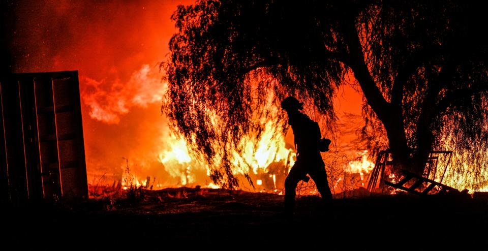 A photojournalist walks among the flames of a wildfire in rural Aguanga on Monday. (The Orange County Register via AP)