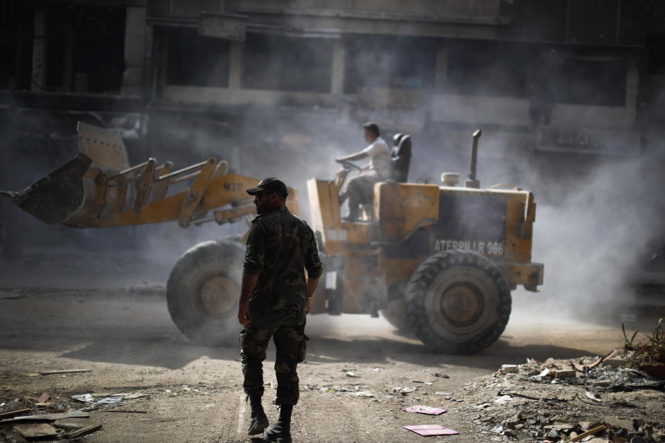 A Syrian soldier directs a bulldozer as removes rubble from damage in street at the Palestinian refugee camp of Yarmouk in the Syrian capital Damascus, Syria, Saturday, Oct. 6, 2018. The camp, once home to the largest concentration of Palestinians outside the territories housing nearly 160,000 people, has been gutted by years of war. (AP Photo/Hassan Ammar)