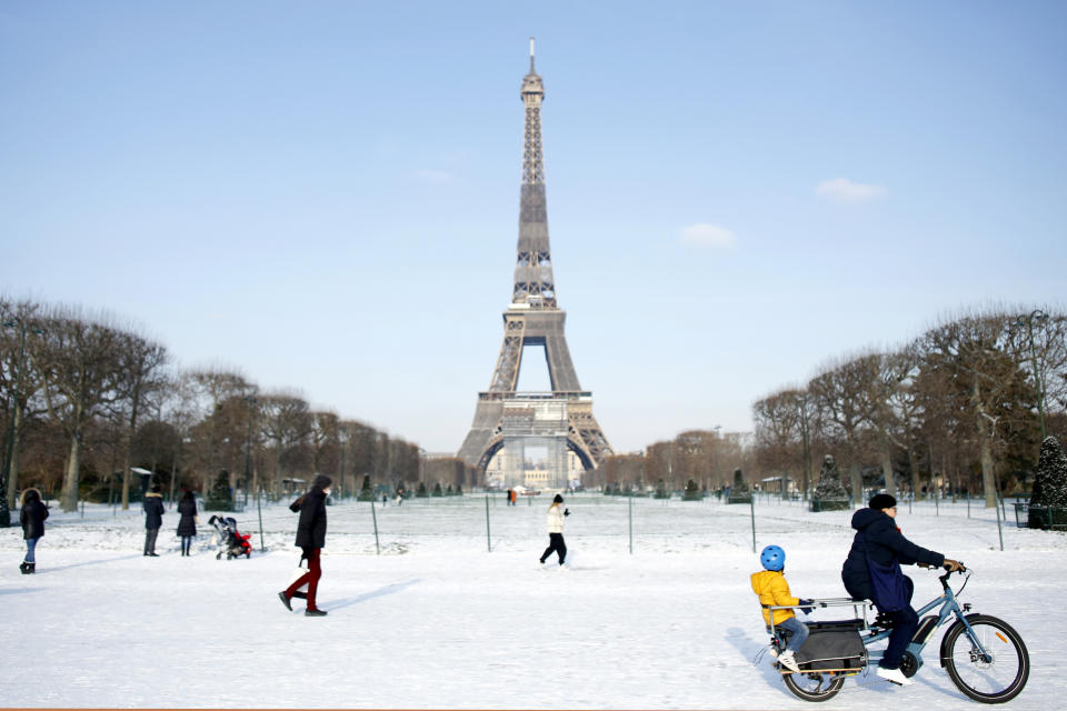 FILE - People walk and ride a bicycle on a snow covered alley near the Eiffel Tower, in Paris, Wednesday, Feb. 10, 2021. Over the quarter century since Paris was regarded as bicycle-unfriendly, the city has taken striking measures to get people on wheels, even subsidizing one third of the cost for people to buy 85,000 electric bikes or cargo bikes from 2009 to 2022. (AP Photo/Thibault Camus, File)