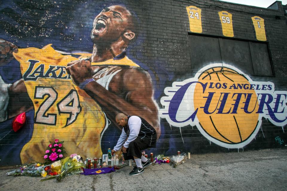 Luis Villanueva lights a candle in front of a Kobe Bryant mural in which he holds up his number 24 jersey beside the words "los angeles culture" written in the font of the Lakers basketball team