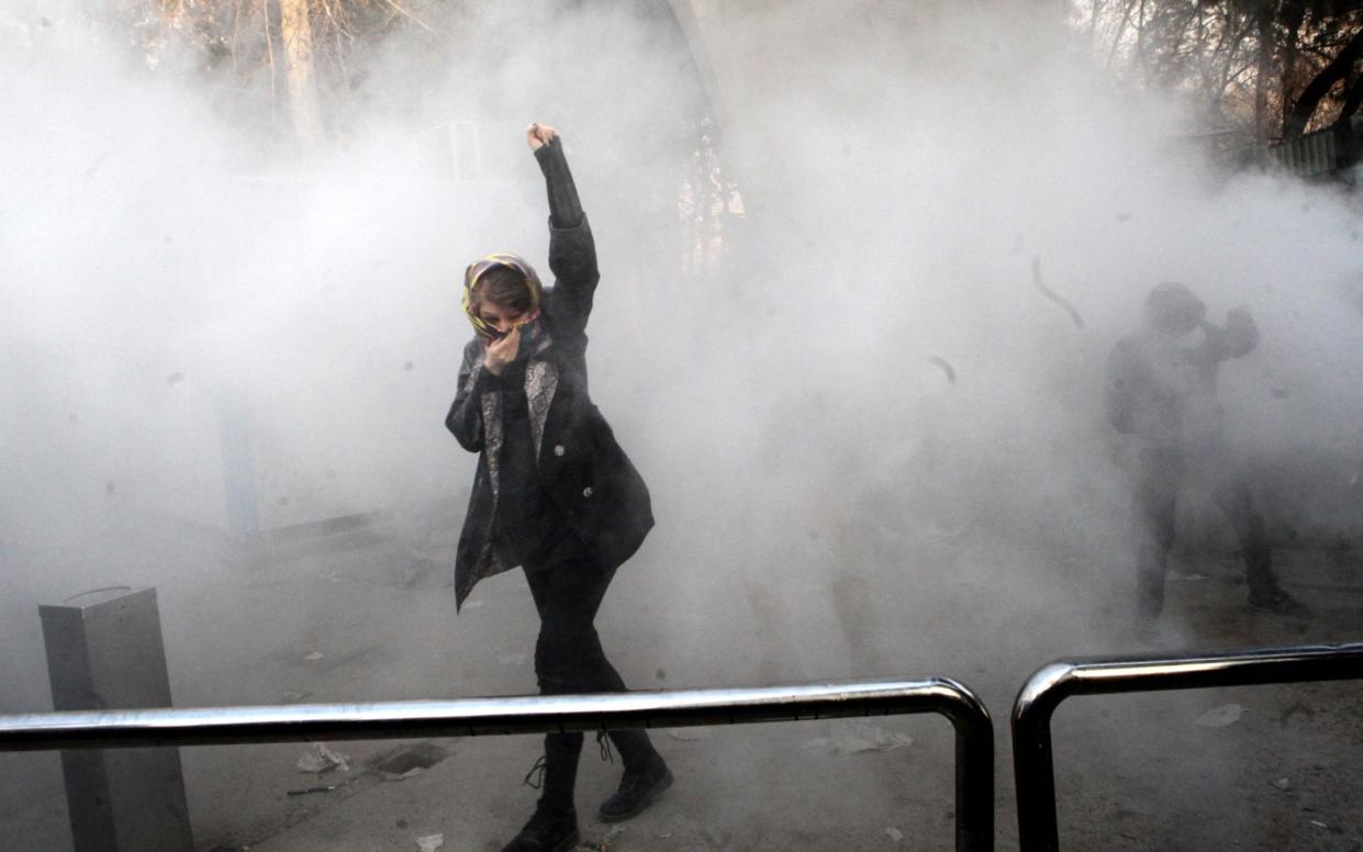 An Iranian woman raises her fist amid the smoke of tear gas at the University of Tehran  - AFP
