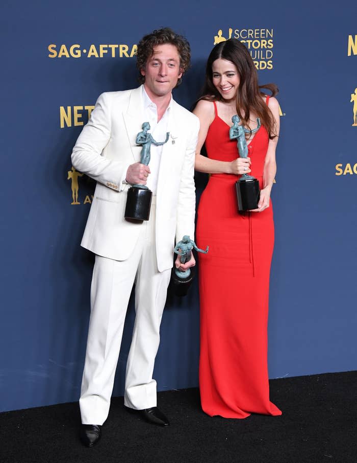 Jeremy Allen White in a suit and Molly Gordon in a red dress holding trophies at the Screen Actors Guild Awards