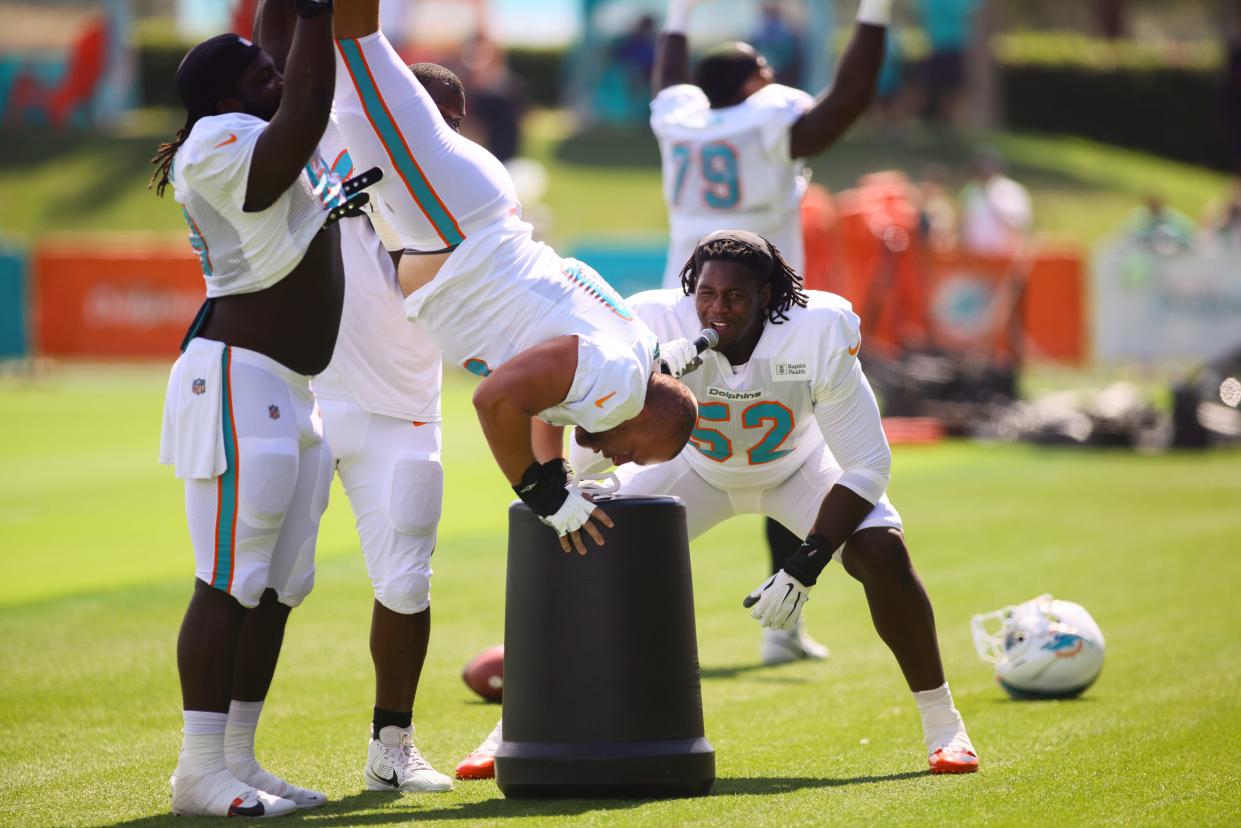 Jul 29, 2024; Miami Gardens, FL, USA; Miami Dolphins offensive tackle Patrick Paul (52) cheers for center Andrew Meyer (60) as Meyer does a handstand over a plastic barrel during training camp at Baptist Health Training Complex. Mandatory Credit: Sam Navarro-USA TODAY Sports