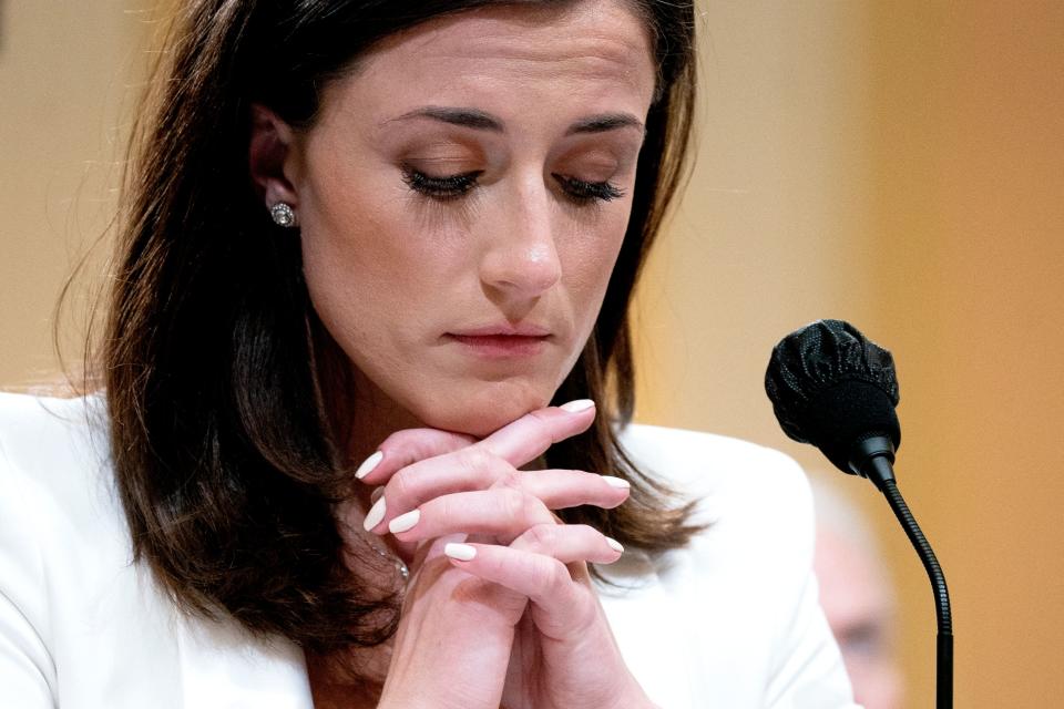 Cassidy Hutchinson looks down while resting her chin on clasped hands in front of a microphone.