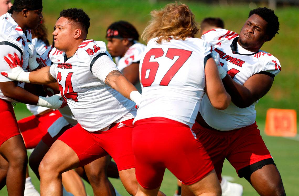 N.C. State’s Chandler Zavala (64), left, and Anthony Belton (74) block while drilling during the Wolfpack’s first practice of fall camp in Raleigh, N.C., Wednesday, August 3, 2022. Belton is blocking Brendan Lawson (67).