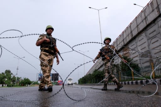 Security personnel stand guard at a roadblock on a deserted street in Jammu, Kashmir