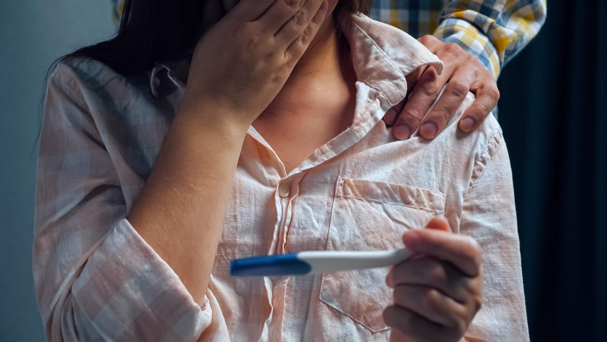 Woman worried holding a pregnancy test with man's hand on her shoulder.