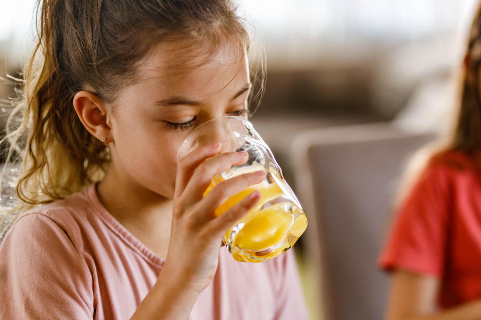 Little girl drinking orange juice from a glass.