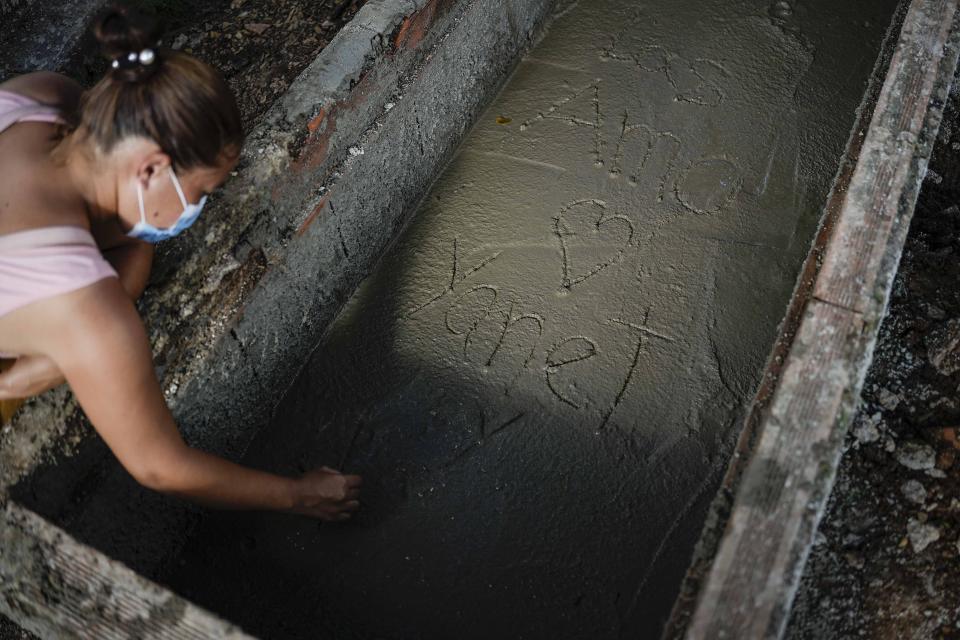 Johaniet Cartaya writes in Spanish "I love you Yanet" on the fresh cement of the grave where her mother Yanet Rivas and aunt Aimara Navas were buried together in Las Tejerias, Venezuela, Wednesday, Oct. 12, 2022. The sisters were among dozens who died when a landslide caused by heavy rains swept Las Tejerias on the night of Oct. 9. (AP Photo/Matias Delacroix)