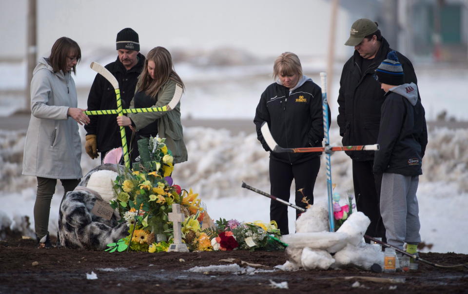 A family places a cross made from hockey sticks at a makeshift memorial at the intersection of a fatal bus crash near Tisdale, Saskatchewan, on Monday. A bus carrying the Humboldt Broncos youth hockey team crashed into a truck en route to Nipawin for a game Friday night, killing 15. (AP/Canadian Press)