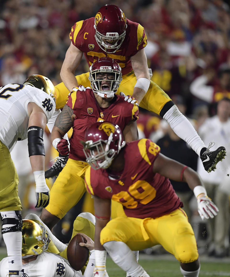 Southern California linebacker Palaie Gaoteote IV, second from top, celebrates after sacking Notre Dame quarterback Ian Book, below, with linebacker Cameron Smith, top, and defensive lineman Christian Rector, second from bottom, stands up during the first half of an NCAA college football game Saturday, Nov. 24, 2018, in Los Angeles. (AP Photo/Mark J. Terrill)