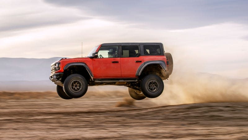 A photo of a red Ford Bronco Raptor SUV jumping over dirt. 