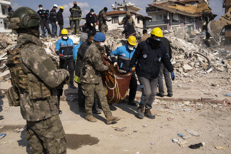 Rescue workers carry a dead person from the rubble of a collapsed building in Antakya, Turkey, Saturday, Feb. 11, 2023. Rescue crews on Saturday pulled more survivors, including entire families, from toppled buildings despite diminishing hopes as the death toll of the enormous quake that struck a border region of Turkey and Syria five days continued to rise. (AP Photo/Petros Giannakouris)