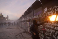 A demonstrator uses fire to attack the police standing behind a barricade protecting the National Palace during a march to commemorate International Women's Day and protesting against gender violence, in Mexico City, Monday, March 8, 2021. (AP Photo/Rebecca Blackwell)