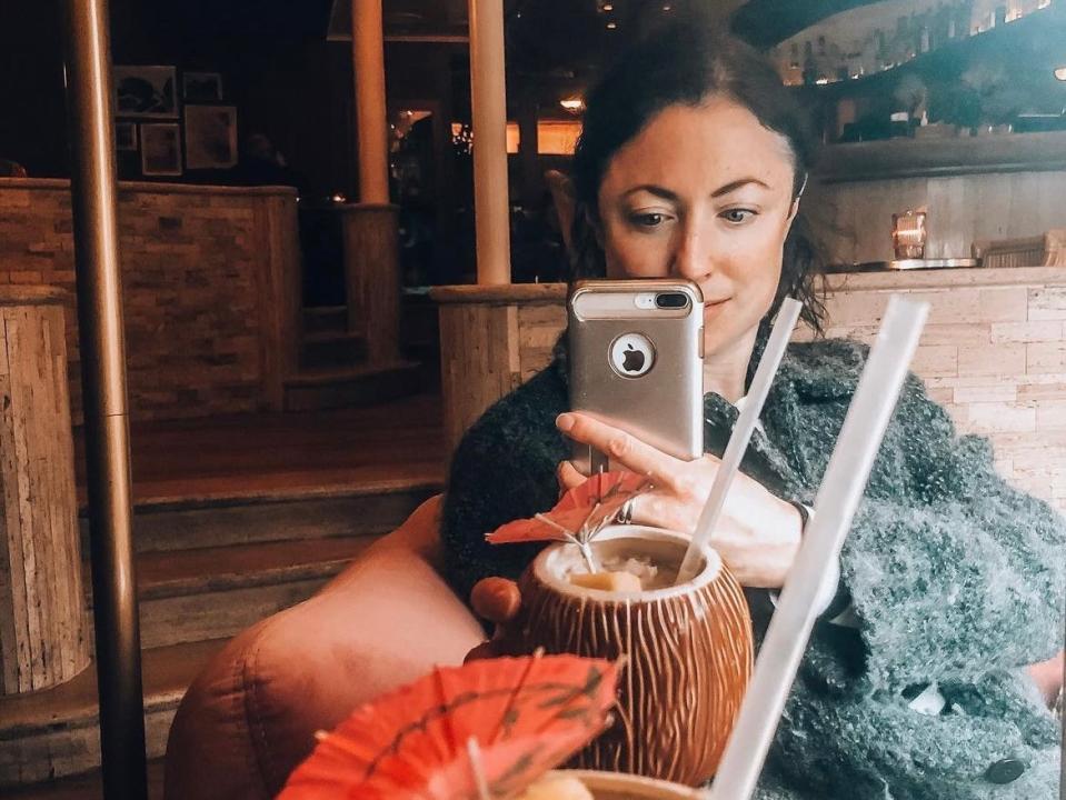 simone posing for a mirror selfie with a craft cocktail in a coconut shaped cup