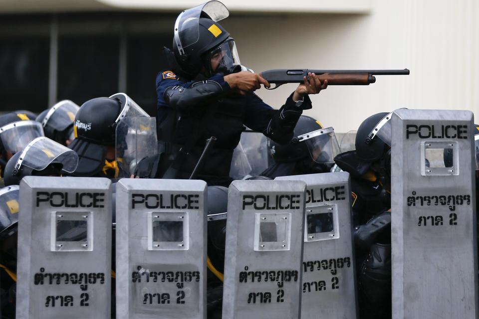 A policeman aims his weapon towards anti-government protesters during clashes near the Government House in Bangkok