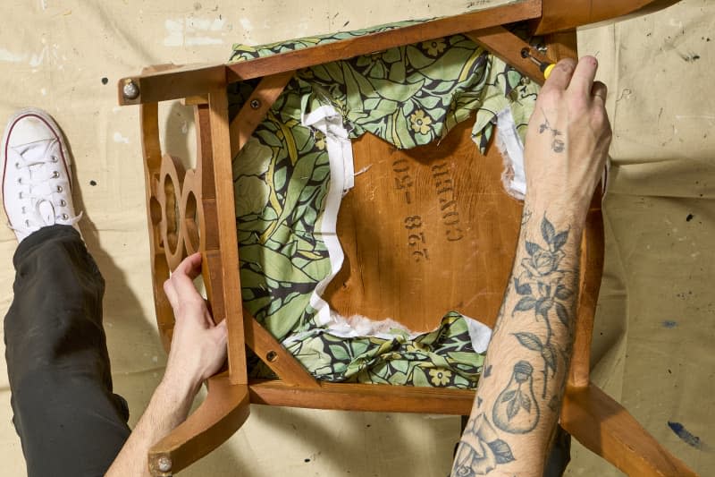 overhead shot of the reupholstered chair being screwed back onto the frame of the chair.