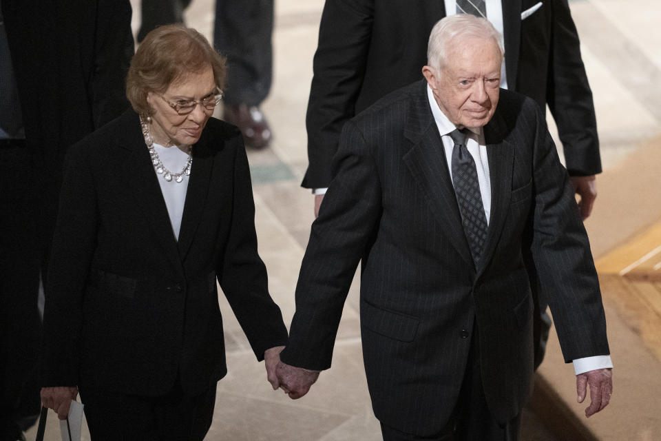 FILE - Former President Jimmy Carter, right, and his wife, former first lady Rosalynn Carter, hold hands as they walk from a state funeral for former President George H.W. Bush at the National Cathedral, Dec. 5, 2018, in Washington. In the year since Jimmy Carter first entered home hospice care, the 39th president has celebrated his 99th birthday, enjoyed tributes to his legacy and outlived his wife of 77 years. Rosalynn Carter, who died in November 2023 after suffering from dementia, spent just a few days under hospice. (AP Photo/Carolyn Kaster, File)
