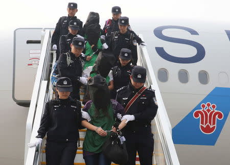 Police escort a group of people wanted for suspected fraud in China, after they were deported from Kenya, as they get off a plane after arriving at Beijing Capital International Airport in Beijing, China, April 13, 2016. REUTERS/Yin Gang/Xinhua