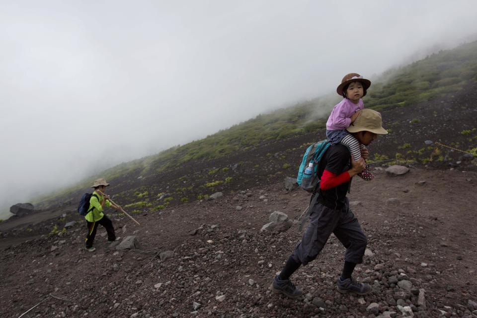 In this Saturday, Aug. 10, 2013 photo, a Japanese man and his children climb one of the trails on Mount Fuji. The recent recognition of the 3,776-meter (12,388-foot) peak as a UNESCO World Heritage site has many here worried that will draw still more people, adding to the wear and tear on the environment from the more than 300,000 who already climb the mountain each year. (AP Photo/David Guttenfelder)