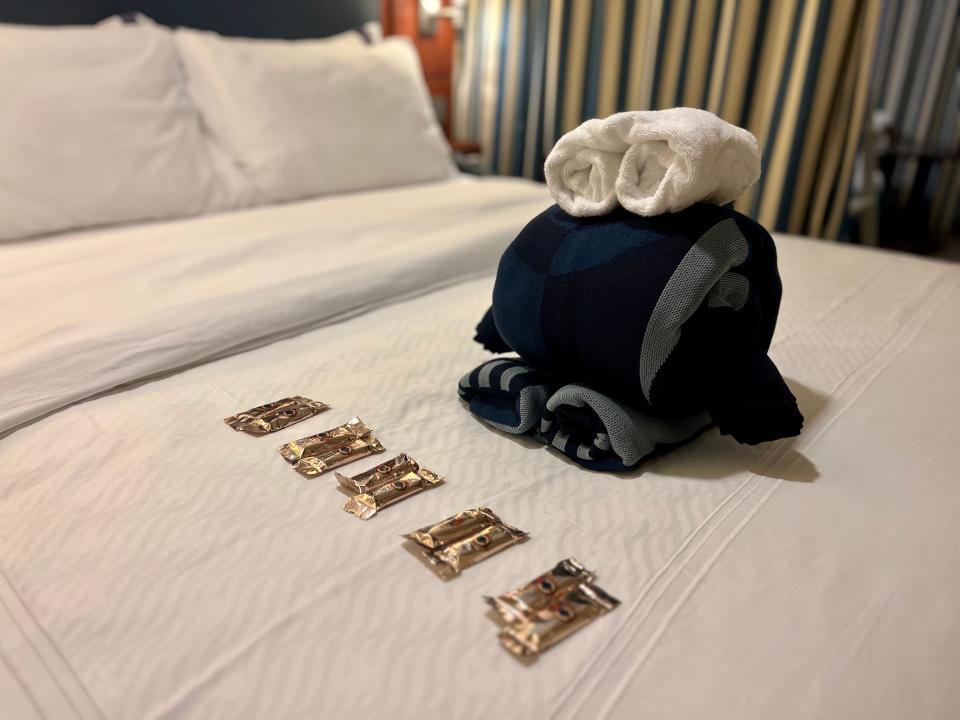 A towel animal folded on the bed with 10 pieces of chocolate.