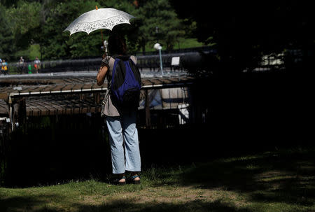 A woman stands under an umbrella during hot weather in Central Park in Manhattan, New York, U.S., June 18, 2018. REUTERS/Shannon Stapleton