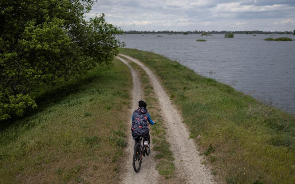 A local resident rides her bike at a flooded area after Ukrainian military forces opened a dam to flood an residencial area in order to stop advance of Russian forces to arrive to the capital city of Kyiv, in Demydiv, Ukraine, May, 15, 2022. - REUTERS/Carlos Barria