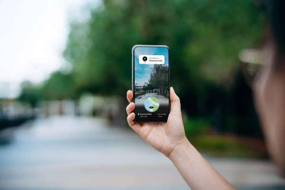 Close up of a woman holding smartphone using an augmented reality application to search for direction to the destination in city street. Following the navigation route with GPS navigation map device. Technology and geolocation concept