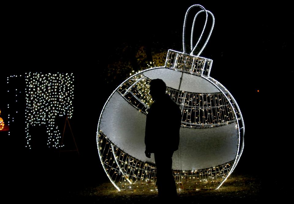 A giant, lighted Christmas ornament design is a backdrop for the silhouette of a visitor to the Luminance light display in 2022 at Mitch Park in Edmond.