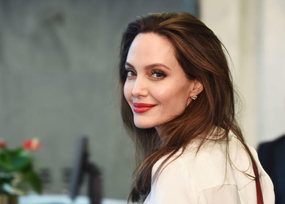 Angelina wears a stylish blouse, poses sideways and looks at the camera with a soft smile