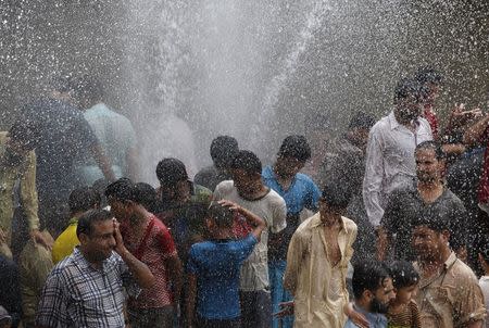 People cool off from the heat as they are sprayed with water jetting out from a leaking water pipeline in Karachi, Pakistan, June 25, 2015. REUTERS/Akhtar Soomro