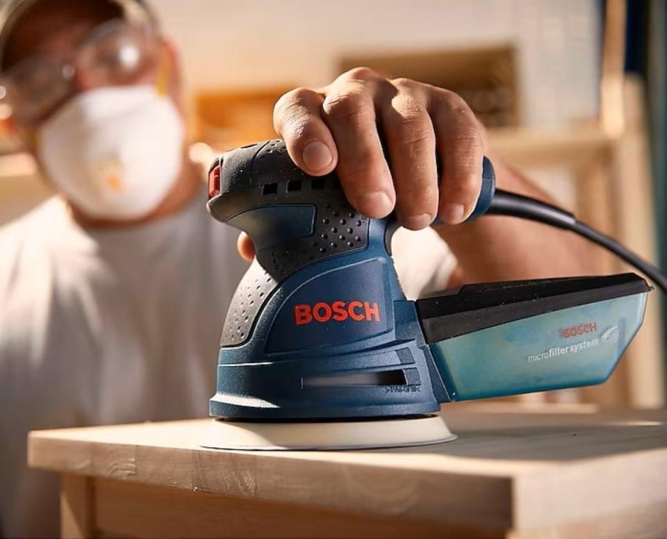 Man holding blue sander to wooden table.