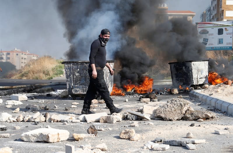 A demonstrator walks near burning tires barricading a road during ongoing anti-government protests in Khaldeh