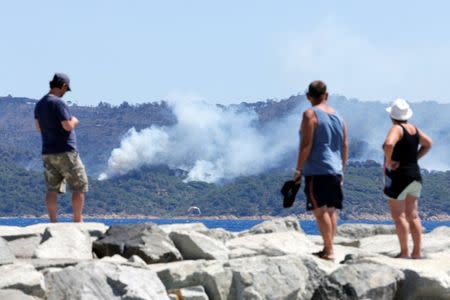 Tourists look smoke that rises from trees at a forest fire on La Croix-Valmer from Cavalaire-sur-Mer, near Saint-Tropez, France, July 25, 2017. REUTERS/Jean-Paul Pelissier