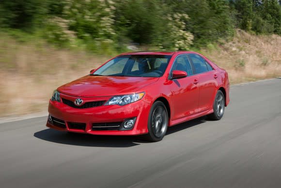 A red Toyota Camry on a road with blurry trees in the background