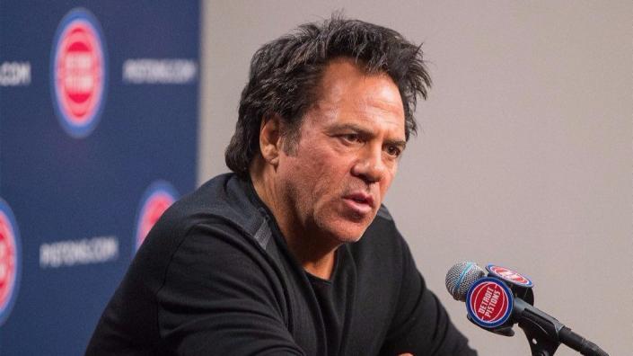 Tom Gores speaks into a microphone at a press conference before logos of the Detroit Pistons