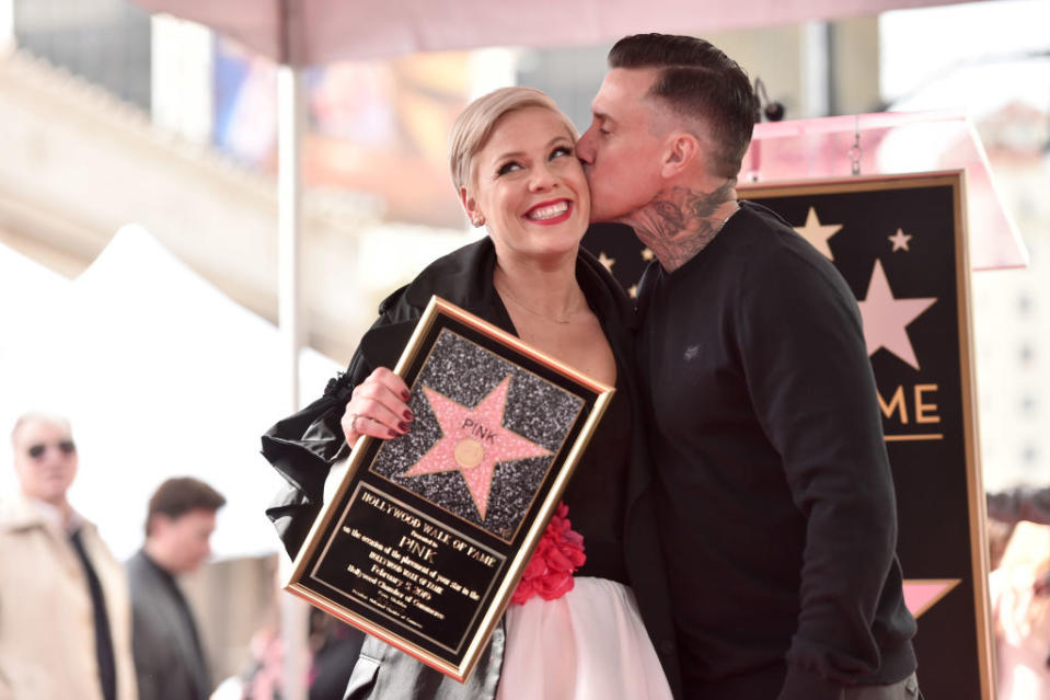 Pink in a white dress receives a kiss on the cheek from Carey, holds a star plaque at Hollywood Walk of Fame ceremony
