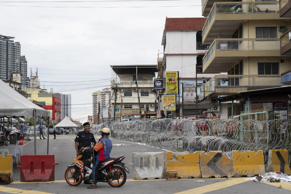 Malaysian Police check a motorcyclist next to barbed wire in the locked down area of Selayang Baru, on the outskirt of Kuala Lumpur, Malaysia, on Sunday, April 26, 2020. The lockdown was implemented to allow authorities to carry out COVID-19 screenings to curb the spread of coronavirus. (AP Photo/Vincent Thian)