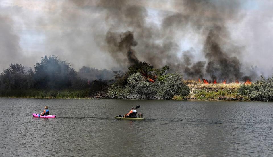 Kayakers Eileen Freeman, left, and Gene Rabung paddle past smoke and flames as Bateman Island burns for the second time this year Wednesday afternoon in Richland.